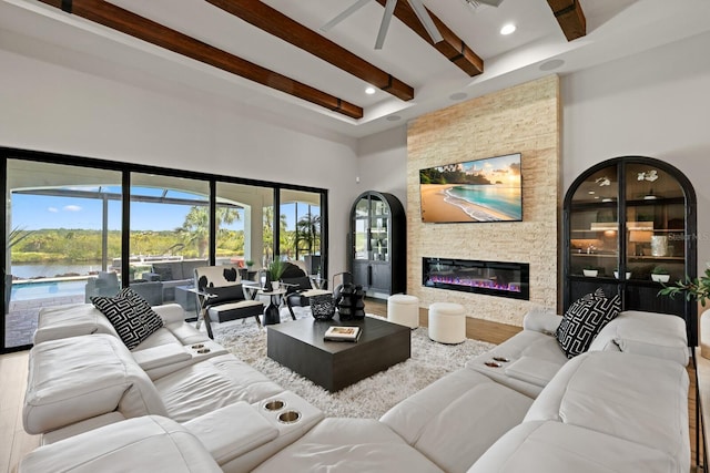 living room with a stone fireplace, beamed ceiling, a water view, and hardwood / wood-style floors