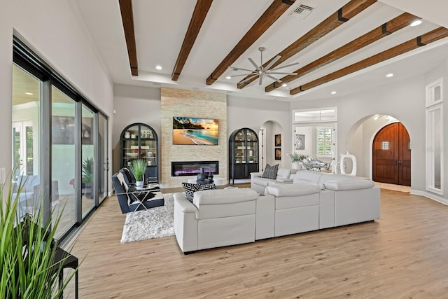 living room featuring a fireplace, light hardwood / wood-style floors, beamed ceiling, and ceiling fan