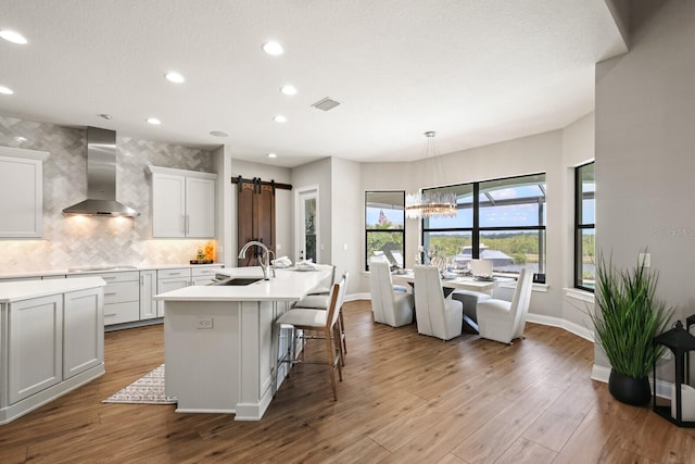 kitchen with a barn door, sink, hardwood / wood-style floors, white cabinets, and wall chimney exhaust hood