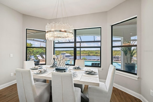 dining area with dark hardwood / wood-style flooring, a wealth of natural light, a chandelier, and a water view