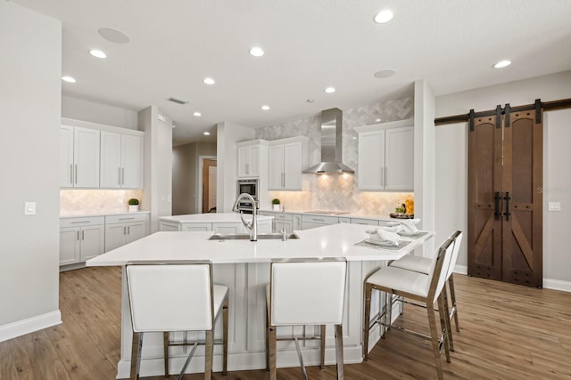 kitchen featuring white cabinetry, light wood-type flooring, a barn door, wall chimney range hood, and a large island