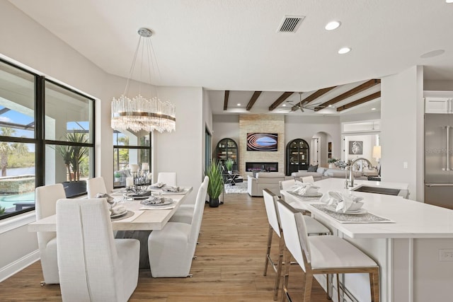 dining room featuring hardwood / wood-style floors, sink, ceiling fan, beam ceiling, and a fireplace