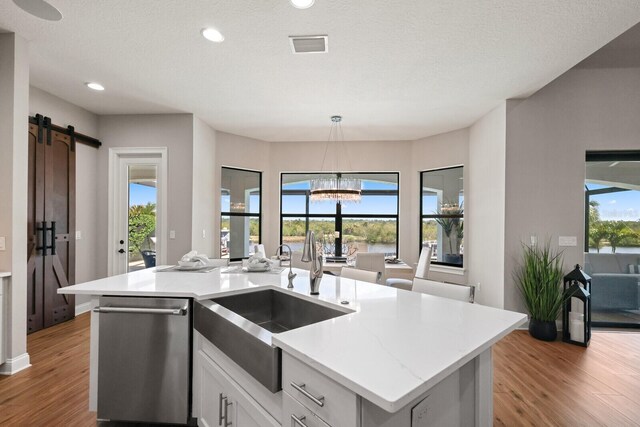 kitchen with white cabinets, stainless steel dishwasher, plenty of natural light, and a center island with sink