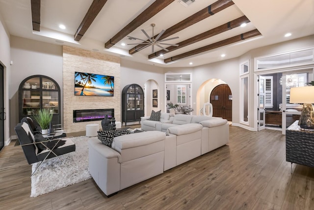 living room featuring beam ceiling, wood-type flooring, ceiling fan, and a fireplace