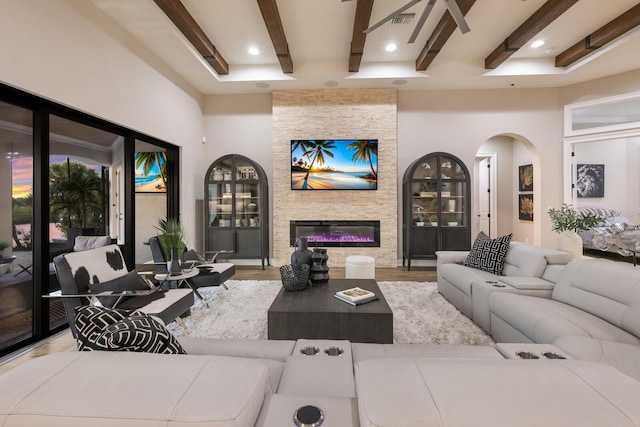 living room featuring a towering ceiling, light wood-type flooring, a fireplace, and beamed ceiling