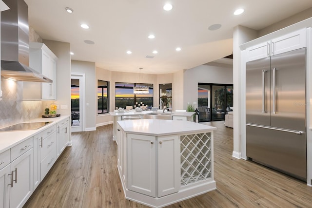 kitchen with stainless steel built in fridge, black electric stovetop, light hardwood / wood-style floors, wall chimney exhaust hood, and a center island