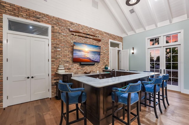 bar featuring high vaulted ceiling, french doors, hardwood / wood-style flooring, and brick wall