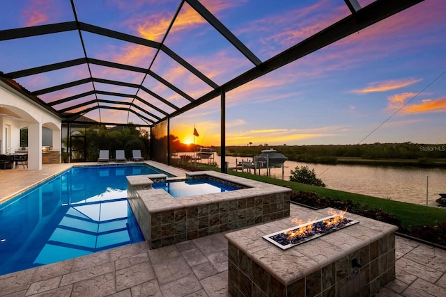 pool at dusk featuring glass enclosure, an in ground hot tub, a patio, a water view, and an outdoor fire pit