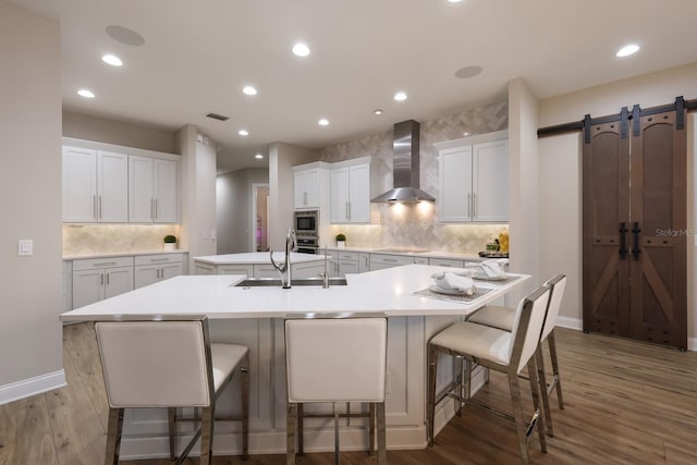 kitchen with wood-type flooring, white cabinets, wall chimney exhaust hood, a barn door, and a spacious island