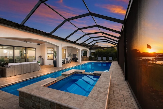 pool at dusk with an in ground hot tub, outdoor lounge area, ceiling fan, a patio, and a lanai