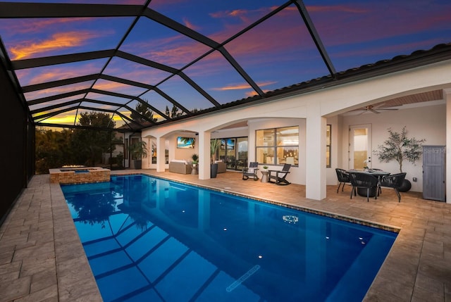 pool at dusk with a patio, glass enclosure, ceiling fan, and an in ground hot tub