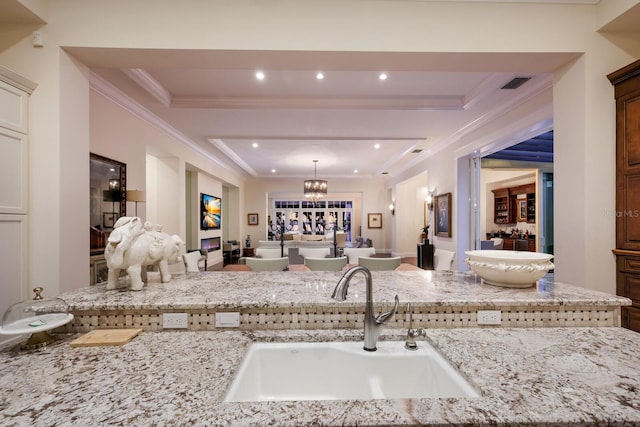 kitchen with an inviting chandelier, light stone counters, hanging light fixtures, and sink