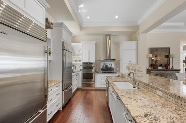 kitchen featuring light stone counters, wall chimney exhaust hood, sink, white cabinetry, and built in fridge