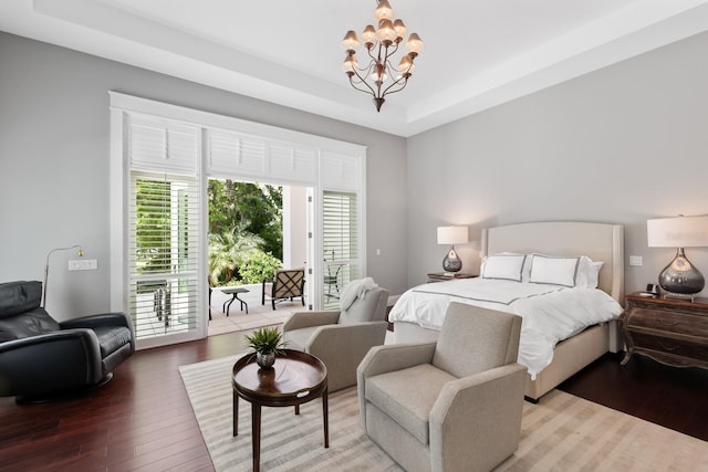 bedroom featuring access to exterior, a tray ceiling, hardwood / wood-style flooring, and a notable chandelier