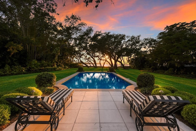 pool at dusk with a yard and a patio