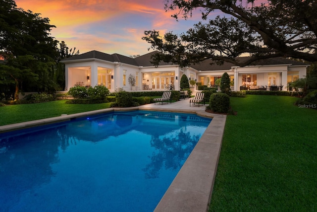 pool at dusk featuring a yard and a patio area