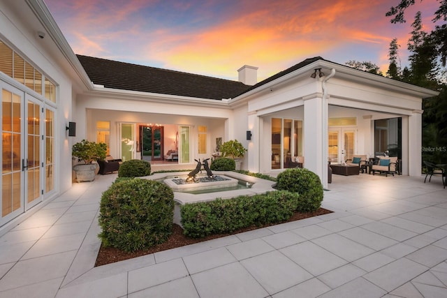 back house at dusk featuring a patio area, french doors, and an outdoor hangout area