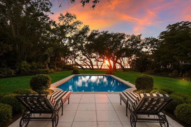 pool at dusk with a yard and a patio area