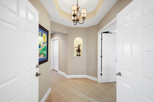 corridor with ornamental molding, a notable chandelier, a raised ceiling, and light wood-type flooring