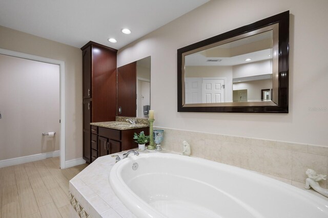 bathroom with wood-type flooring, oversized vanity, and tiled bath