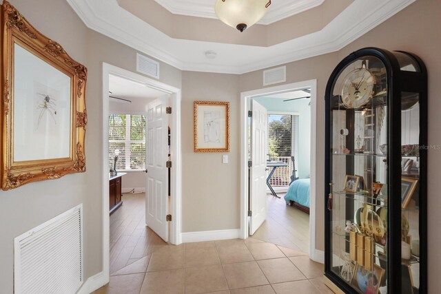 corridor with ornamental molding, light tile floors, and a raised ceiling