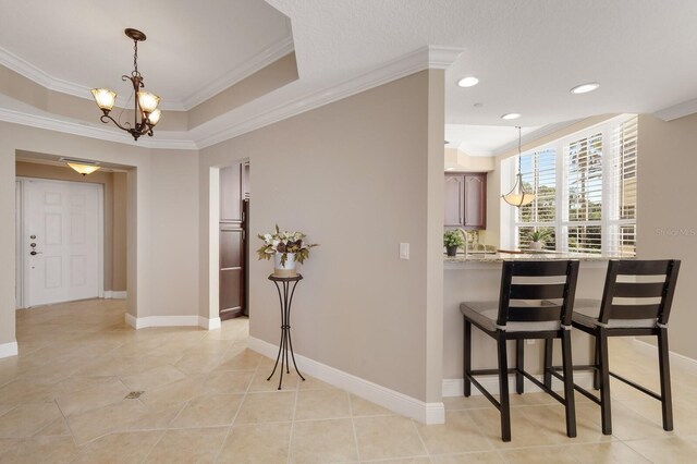 kitchen with a breakfast bar area, a raised ceiling, crown molding, and light tile floors