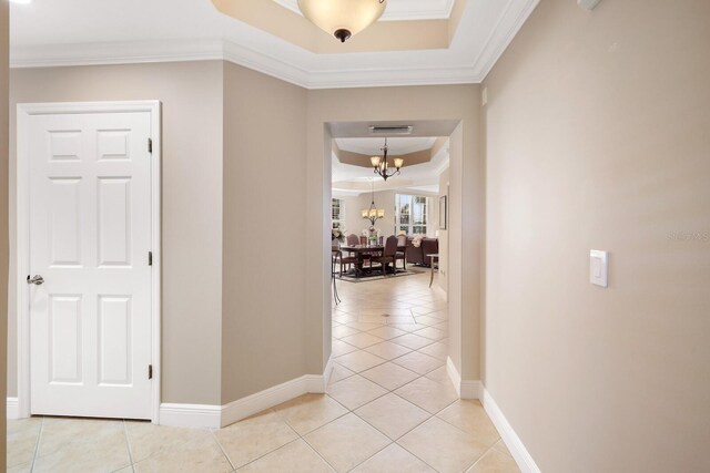 hallway featuring ornamental molding, light tile flooring, a tray ceiling, and an inviting chandelier