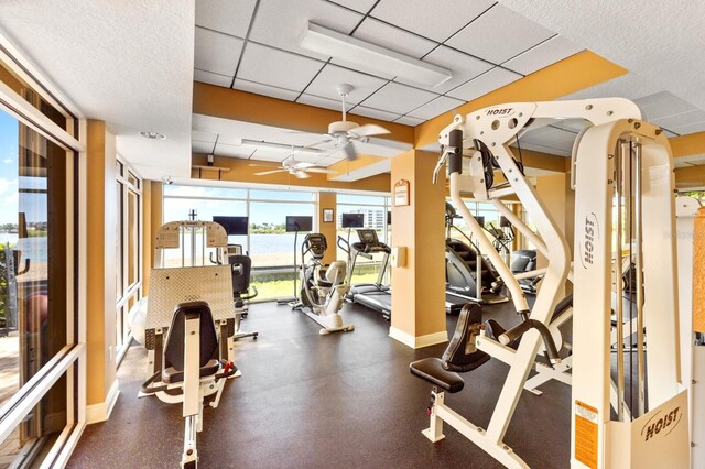 gym with a drop ceiling, ceiling fan, and a water view