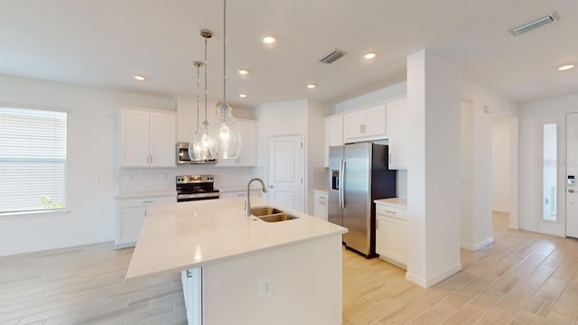 kitchen featuring white cabinets, hanging light fixtures, sink, an island with sink, and appliances with stainless steel finishes