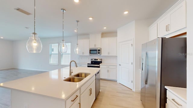 kitchen featuring sink, hanging light fixtures, stainless steel appliances, light hardwood / wood-style flooring, and an island with sink