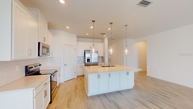 kitchen featuring white cabinetry, hanging light fixtures, stainless steel appliances, a center island with sink, and light wood-type flooring