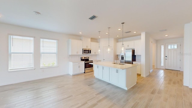 kitchen featuring a center island with sink, white cabinets, sink, light hardwood / wood-style flooring, and appliances with stainless steel finishes