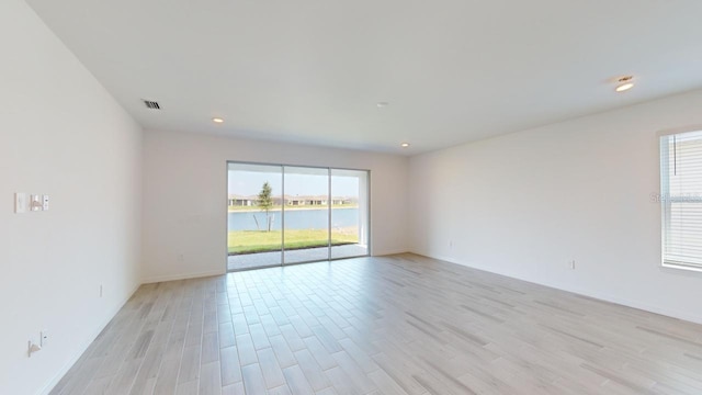 unfurnished room featuring light wood-type flooring, a water view, and plenty of natural light