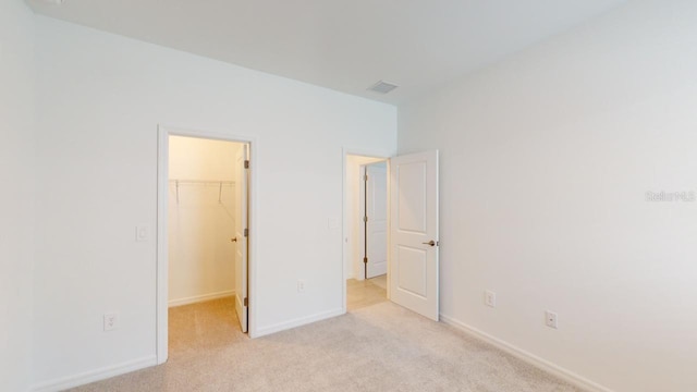 unfurnished bedroom with light carpet, a spacious closet, and a closet