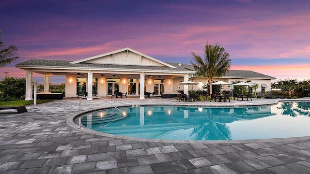 pool at dusk featuring ceiling fan and a patio