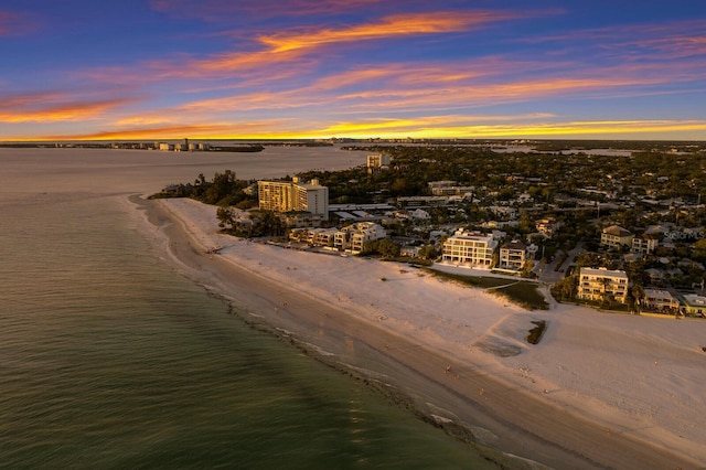 aerial view at dusk featuring a water view and a beach view