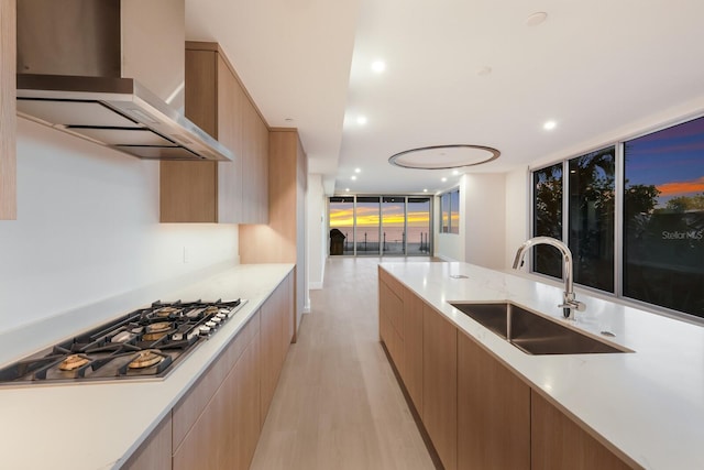 kitchen with wall chimney exhaust hood, stainless steel gas cooktop, light wood-type flooring, sink, and floor to ceiling windows