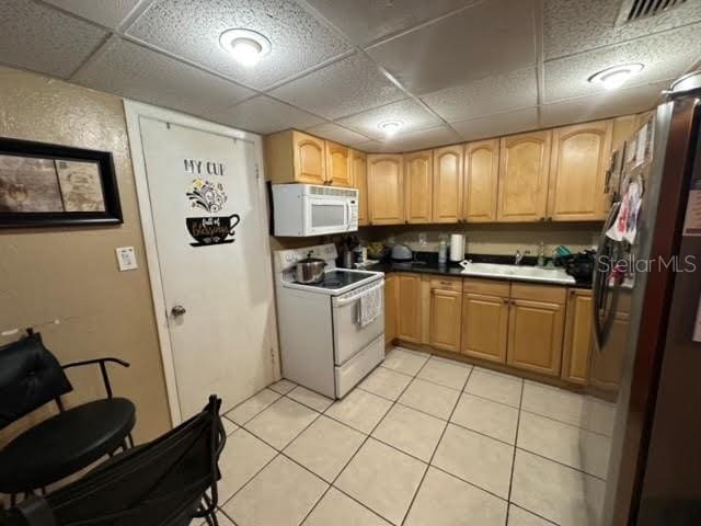 kitchen featuring a drop ceiling, sink, white appliances, and light tile floors