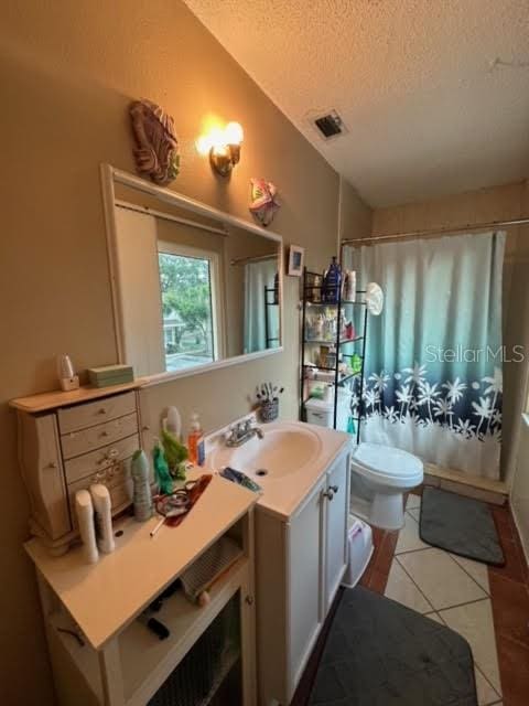 bathroom featuring tile floors, vanity, toilet, and a textured ceiling