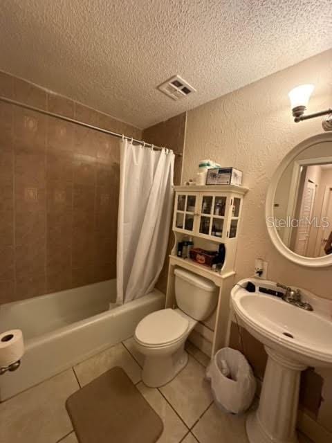 bathroom with a textured ceiling, tile floors, shower / bathtub combination with curtain, and toilet