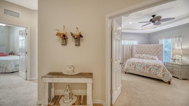 bedroom featuring ceiling fan, light carpet, and a tray ceiling