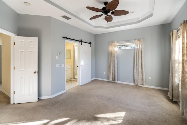 unfurnished bedroom featuring light carpet, ensuite bath, a tray ceiling, ceiling fan, and a barn door