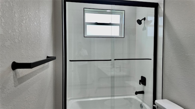 bathroom featuring combined bath / shower with glass door and toilet