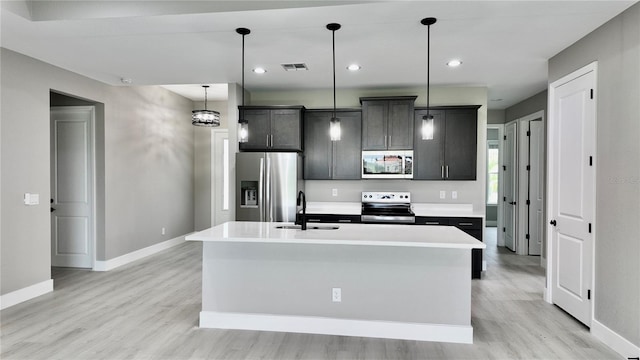 kitchen with appliances with stainless steel finishes, a kitchen island with sink, sink, and light hardwood / wood-style flooring