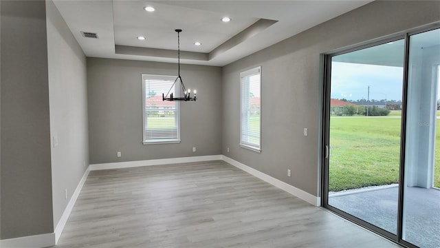 unfurnished dining area featuring a chandelier, light hardwood / wood-style floors, and a raised ceiling