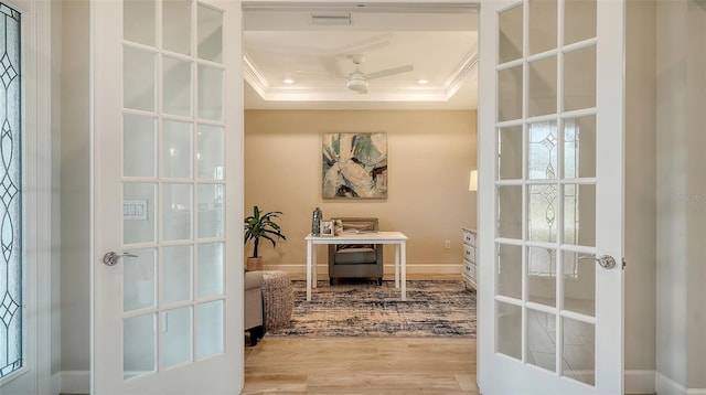 entryway with ceiling fan, french doors, a raised ceiling, hardwood / wood-style flooring, and ornamental molding