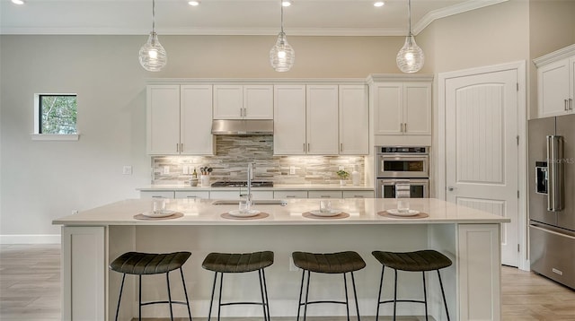 kitchen with pendant lighting, appliances with stainless steel finishes, white cabinetry, an island with sink, and decorative backsplash