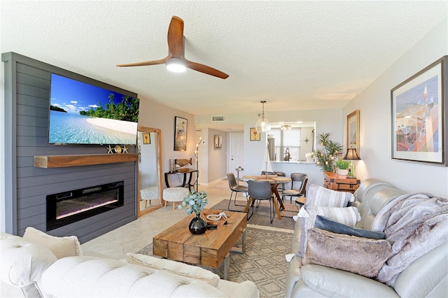 living room with a textured ceiling, a large fireplace, and ceiling fan