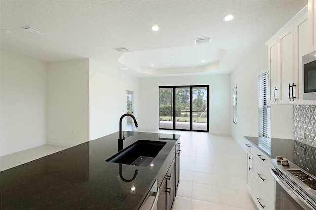 kitchen with a raised ceiling, sink, dark stone countertops, a textured ceiling, and white cabinetry