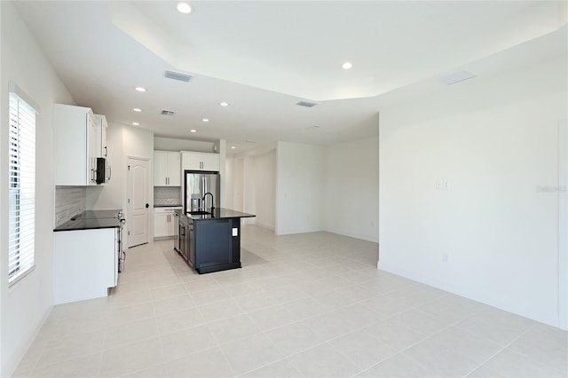 kitchen with decorative backsplash, a kitchen island with sink, light tile patterned floors, stainless steel fridge with ice dispenser, and white cabinetry